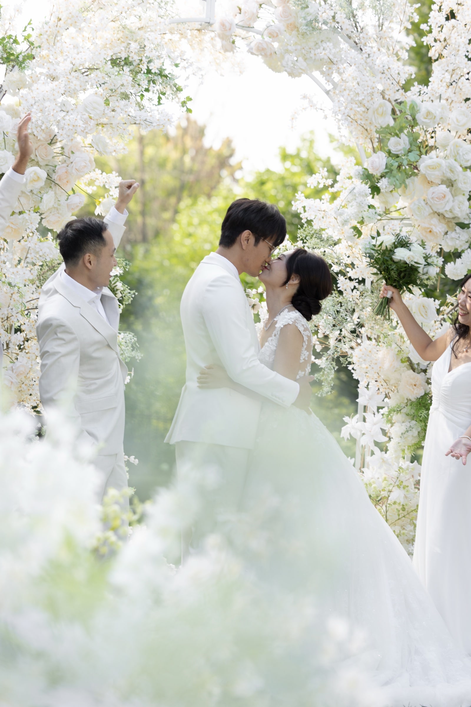 The first kiss beneath a white floral arch at an outdoor garden ceremony