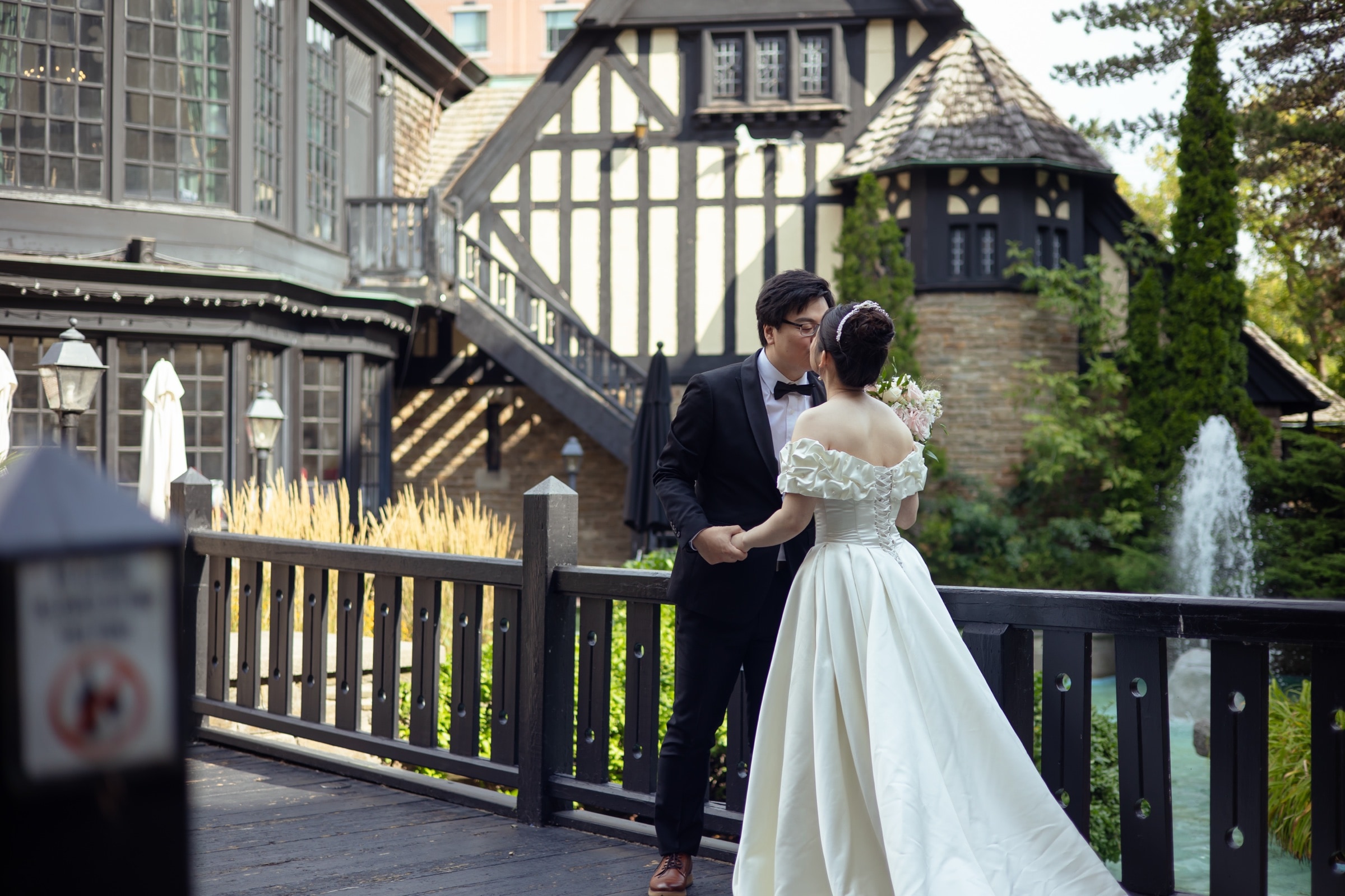 Bride and groom on a garden bridge before the Tudor stone tower at Old Mill Toronto