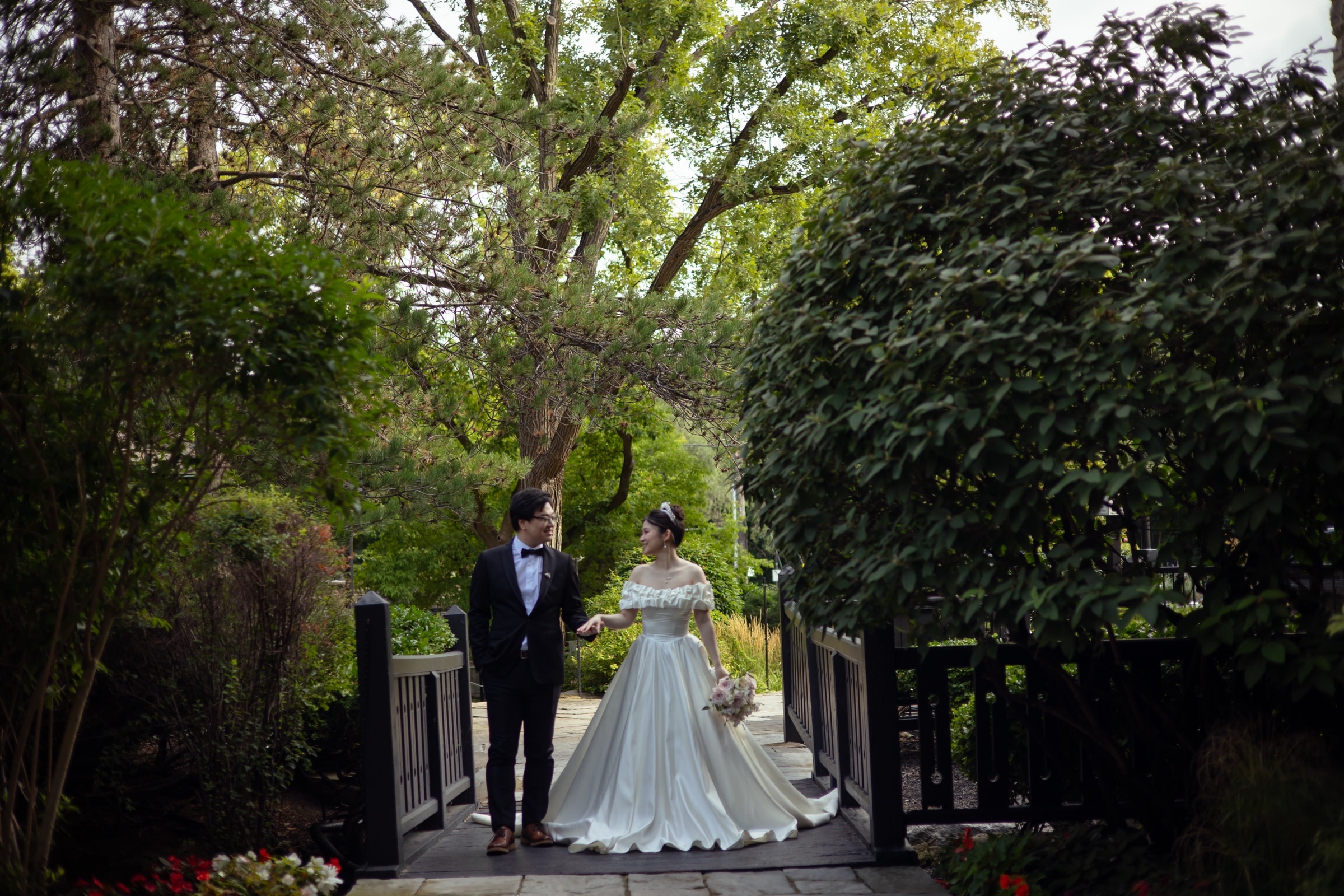The couple holding hands on a garden bridge surrounded by greenery