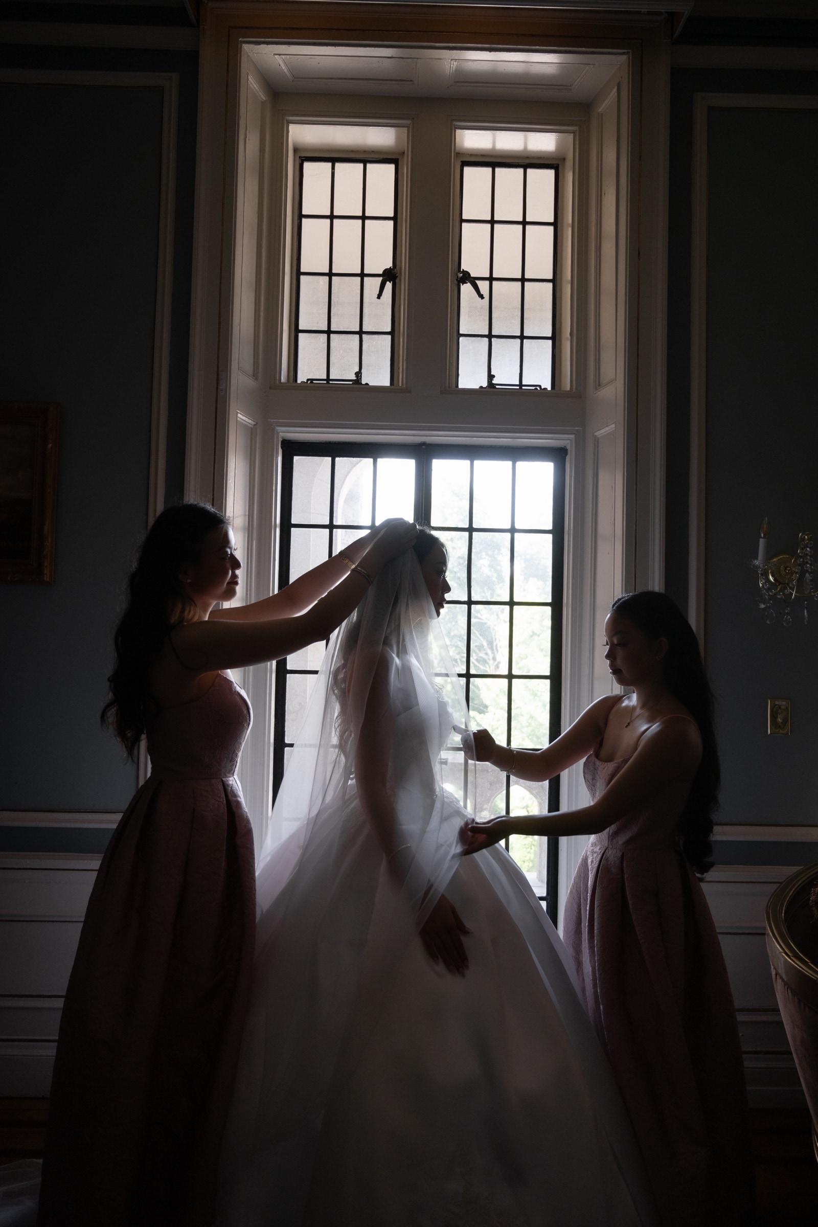 The bride in silhouette at a window with her bridesmaids