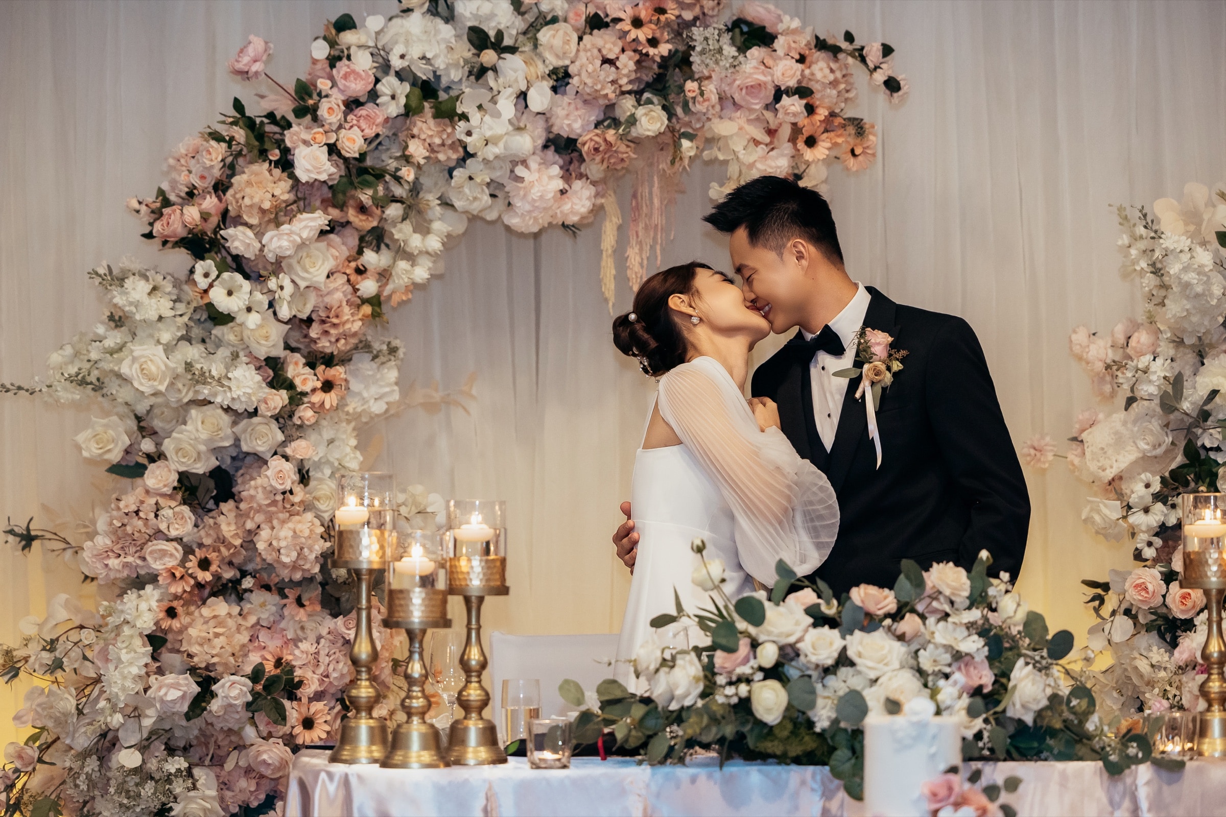 The couple kissing at the blush floral arch