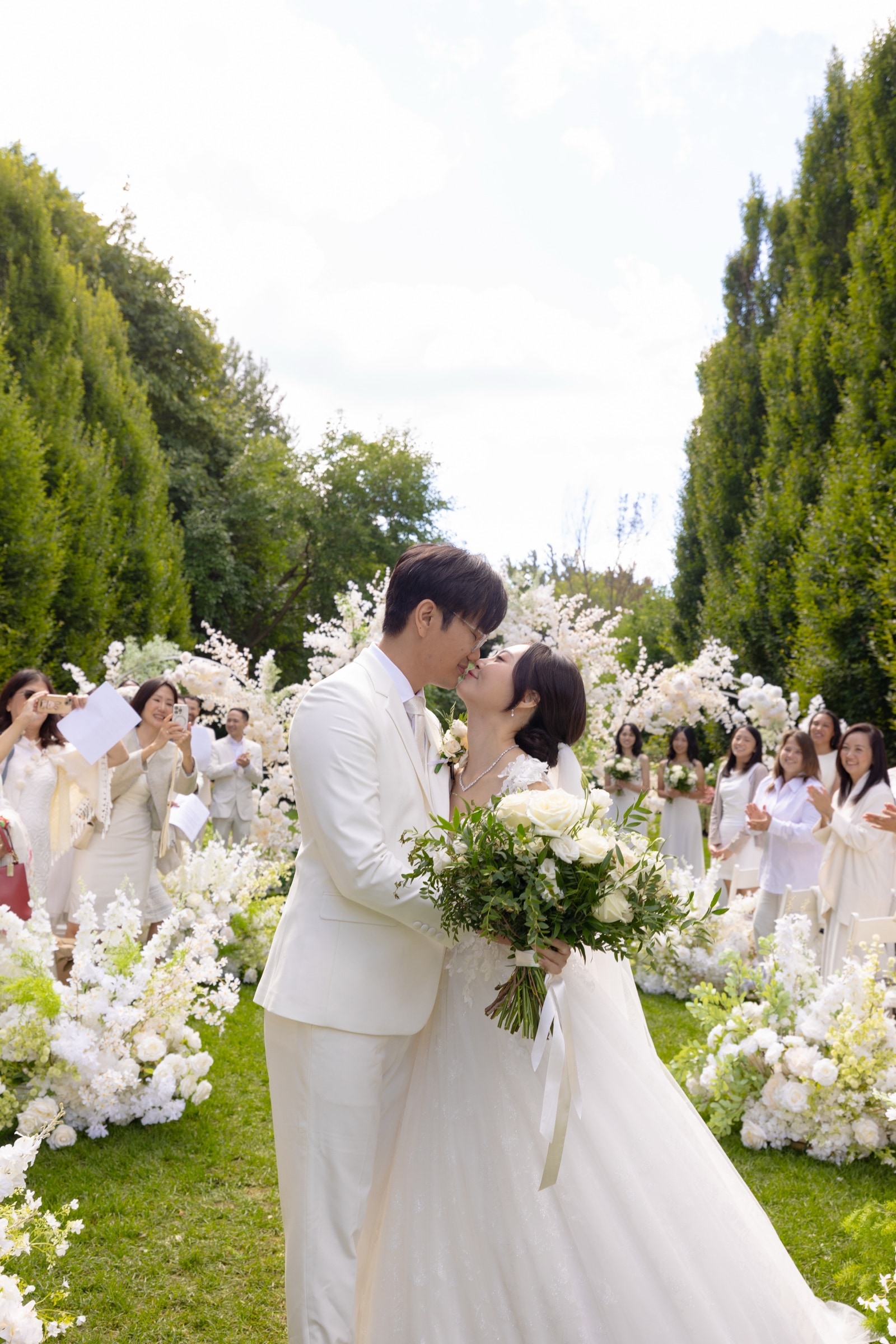 The couple kissing as guests in white look on in the garden