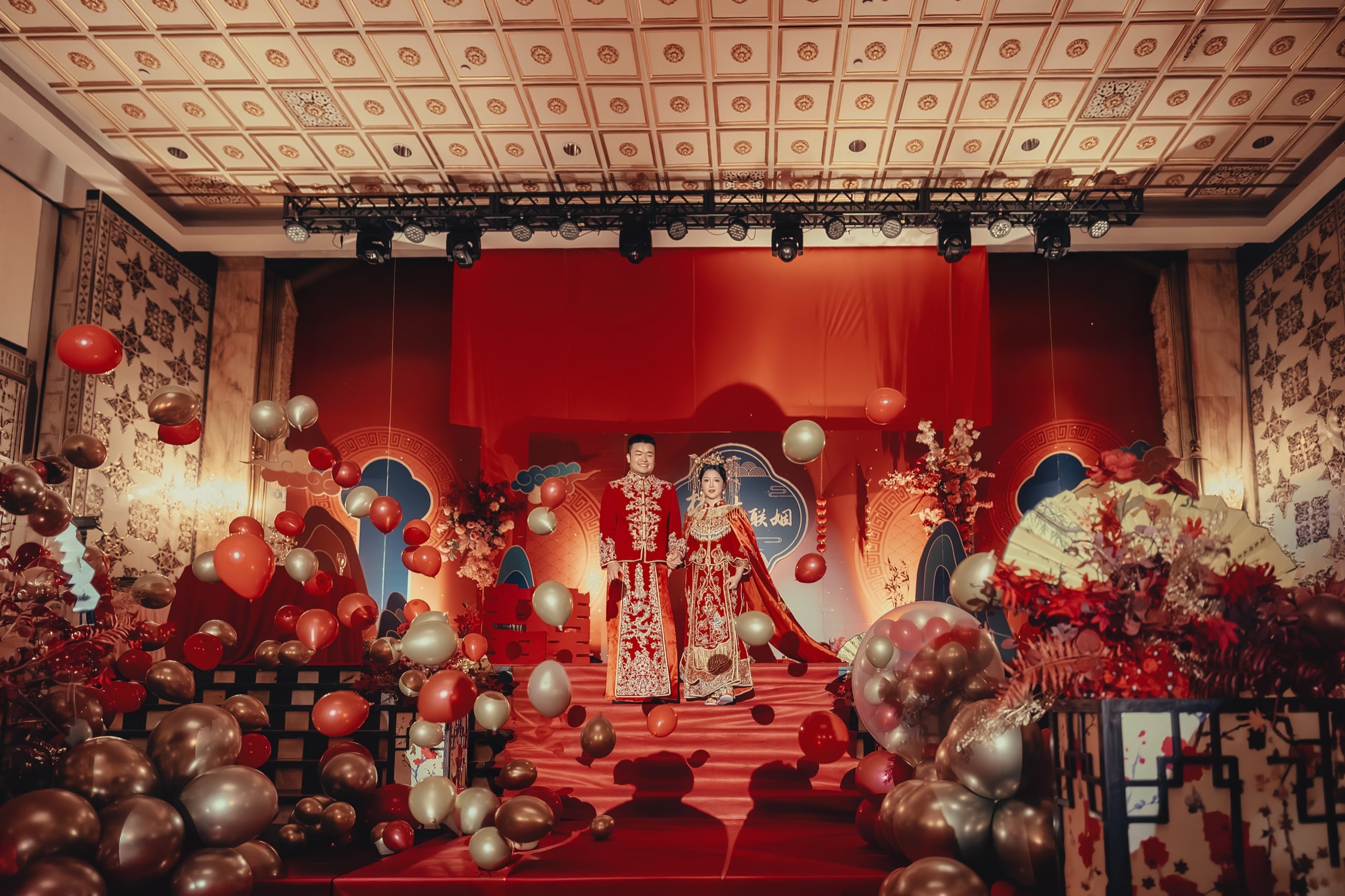 Couple in red ceremonial attire on the wedding stage with red-and-gold balloons — Orchid Photo, GTA Chinese wedding