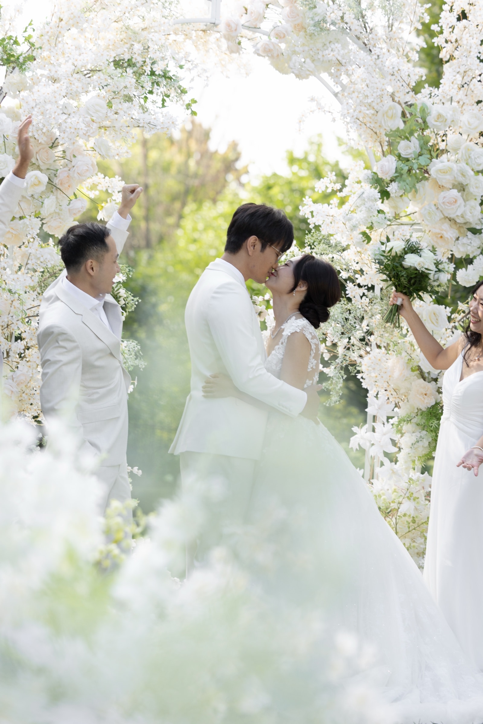 The first kiss beneath a white floral arch at an outdoor garden ceremony