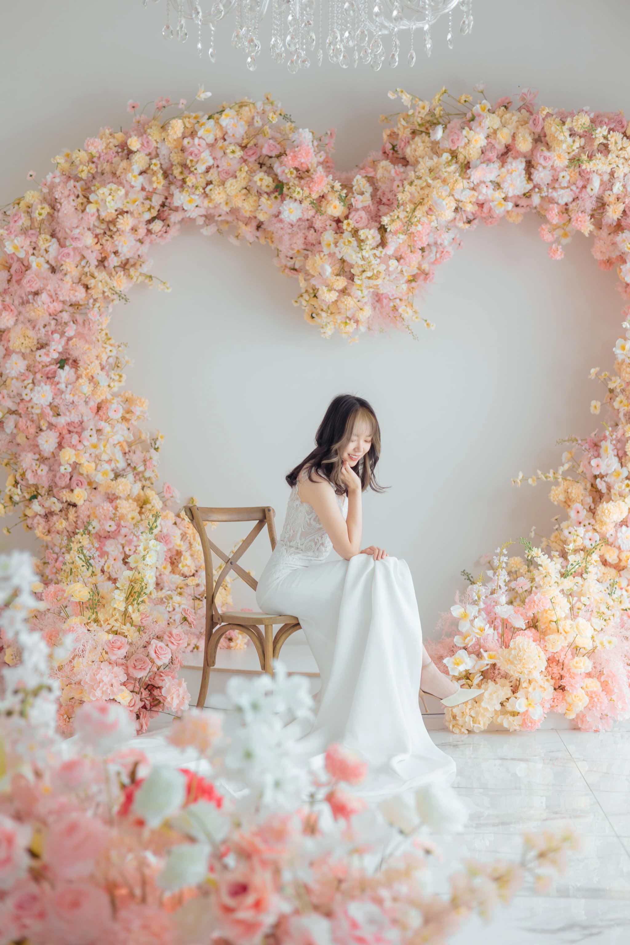 A woman seated on a chair inside a heart-shaped floral arch