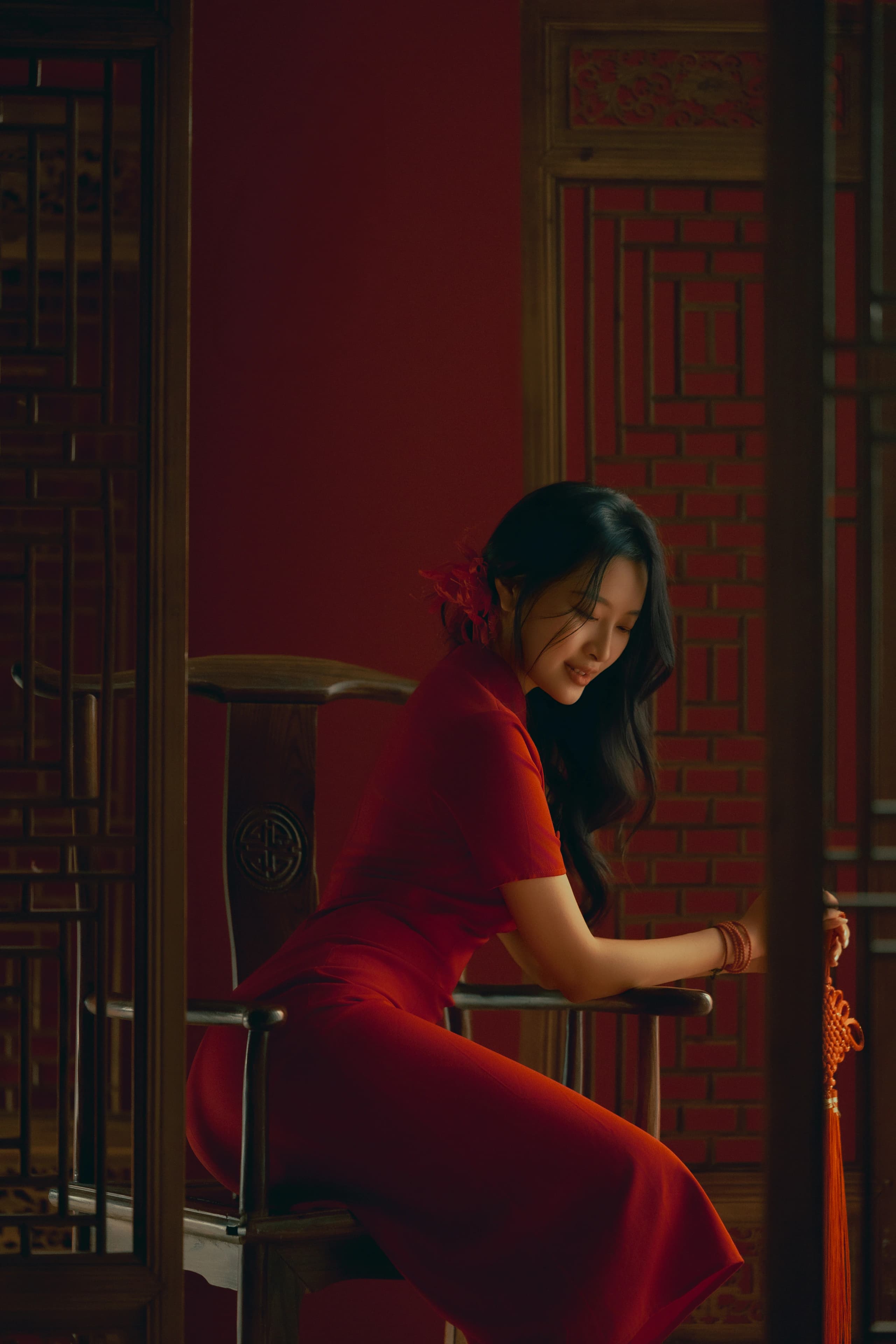 A woman in a fitted red Chinese dress seated by a red lattice door