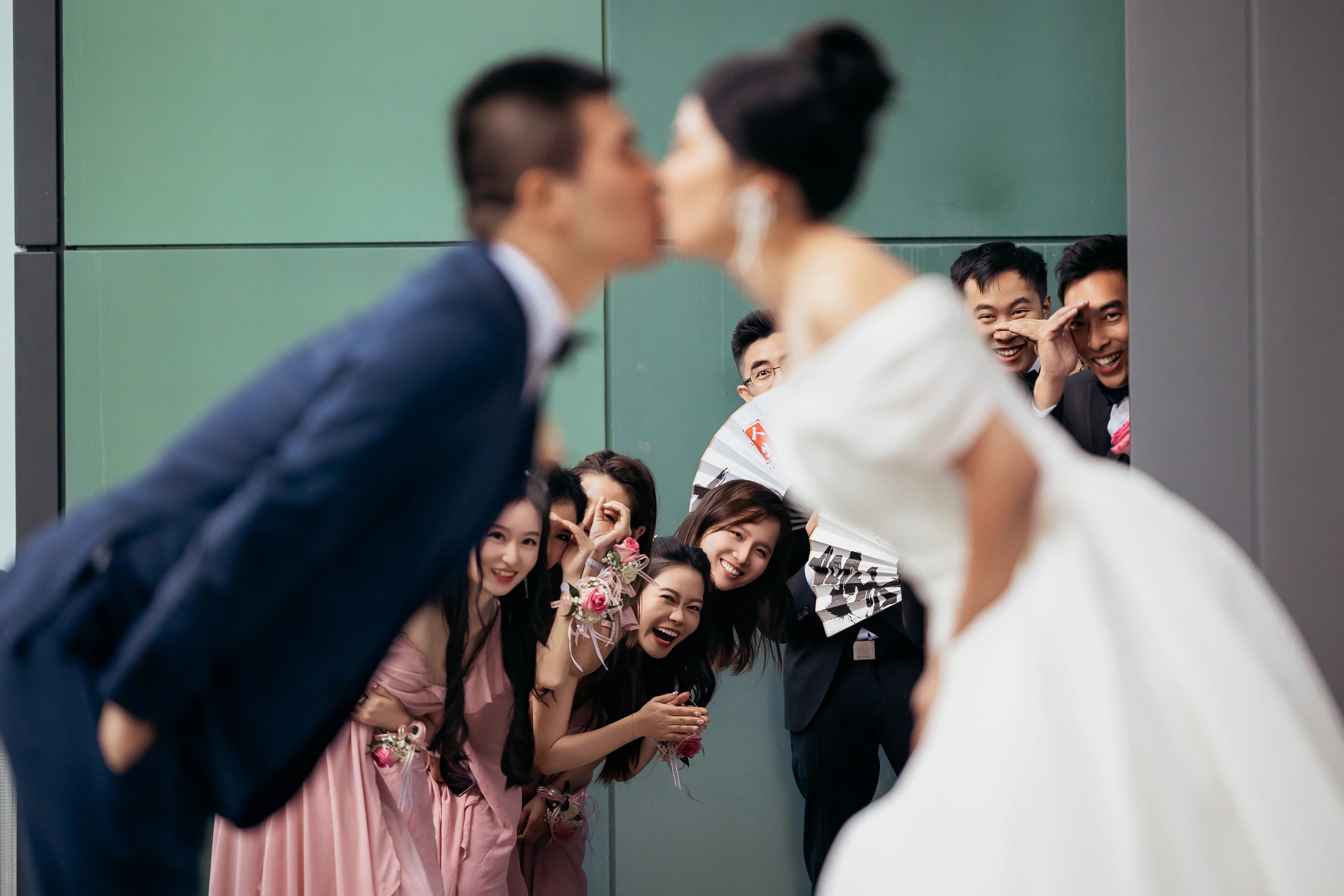 The couple kissing as the wedding party peer around them