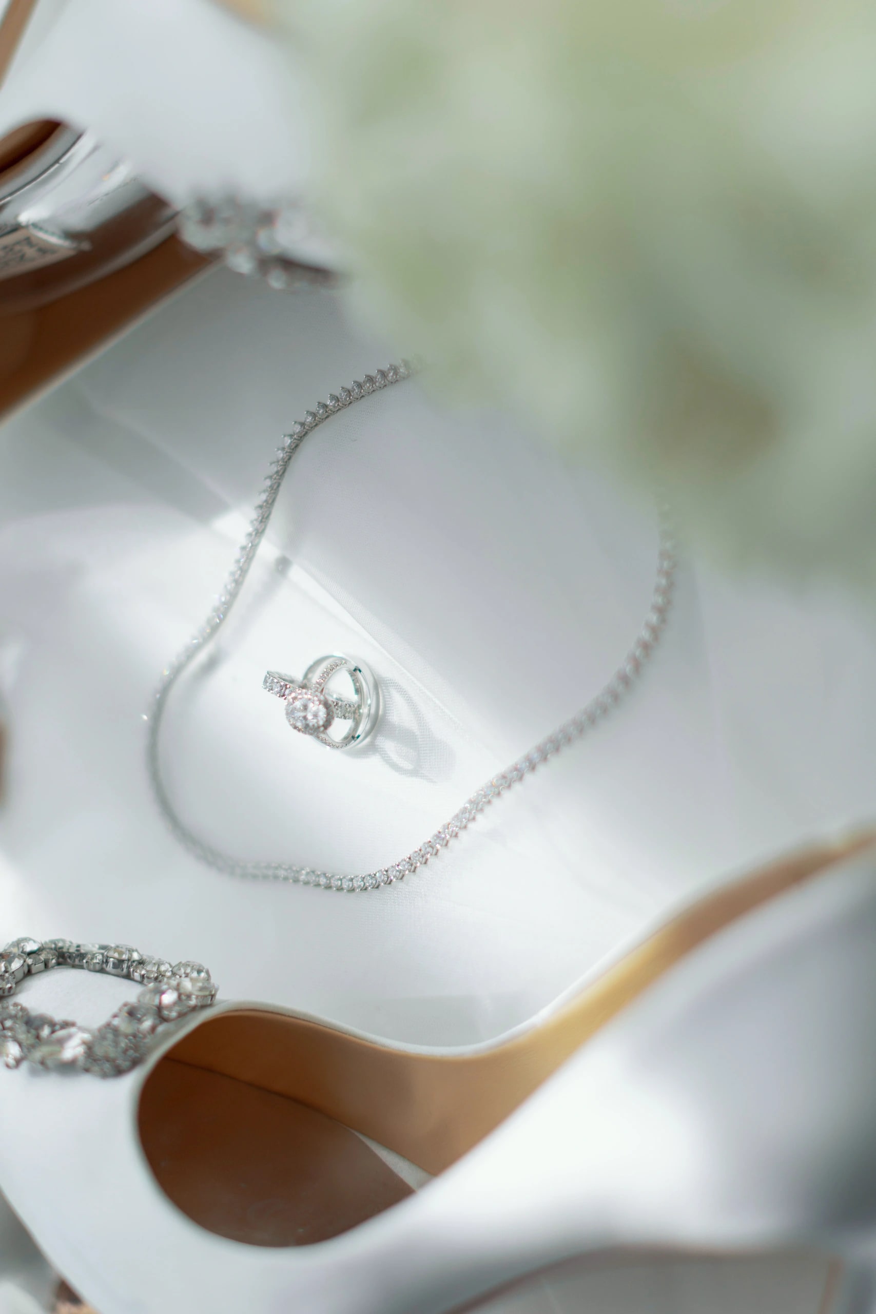 The wedding rings and a diamond necklace laid on a white heel with a crystal buckle