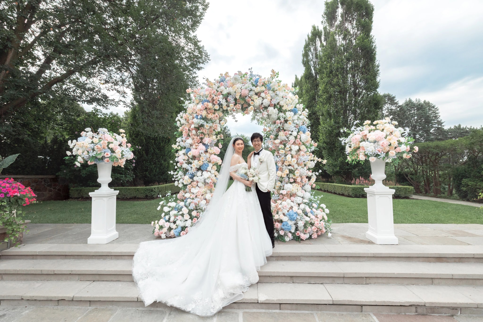 The couple on the stone steps in front of the floral arch, the bride's train spread down the steps