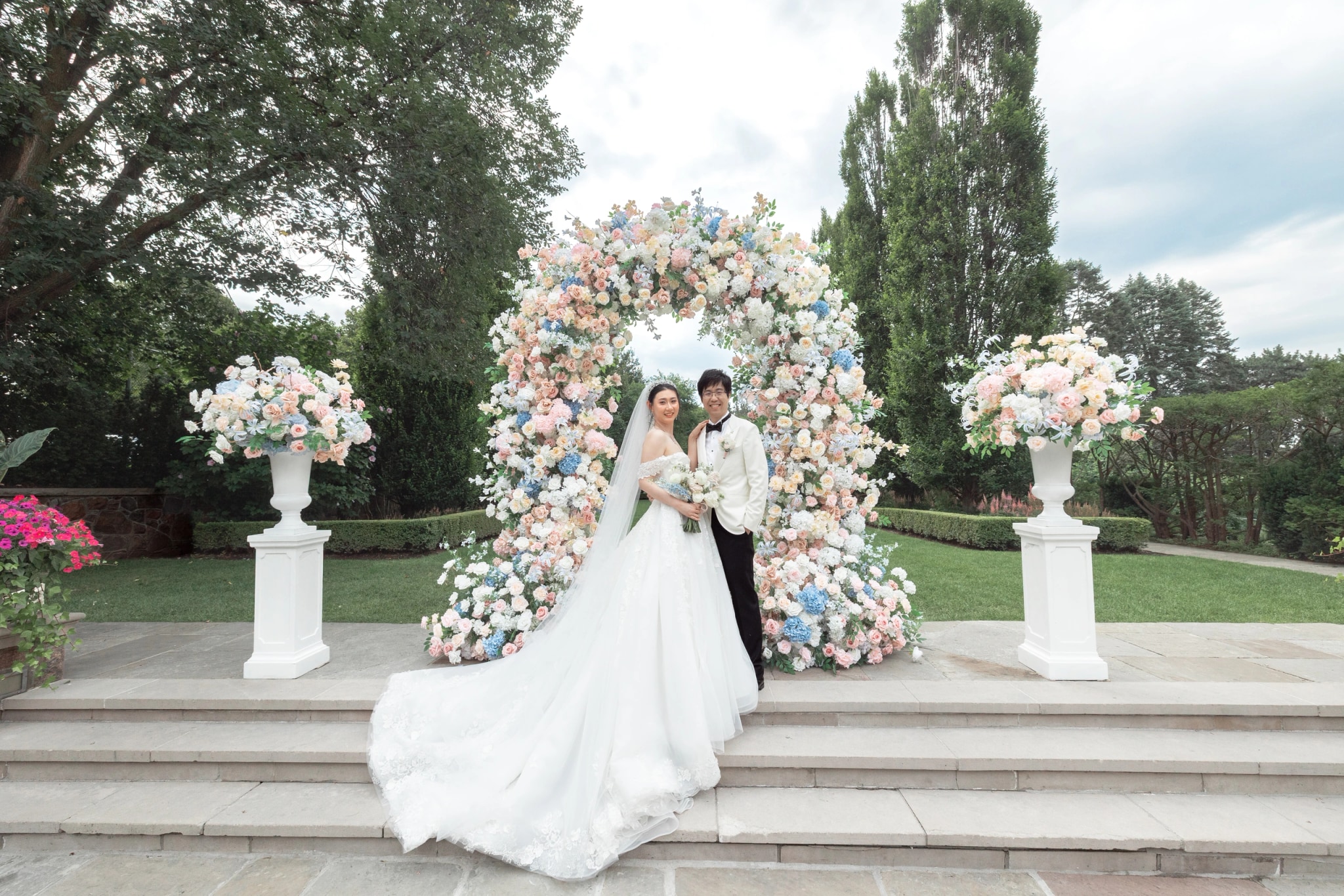 The couple on the stone steps in front of the floral arch, the bride's train spread down the steps
